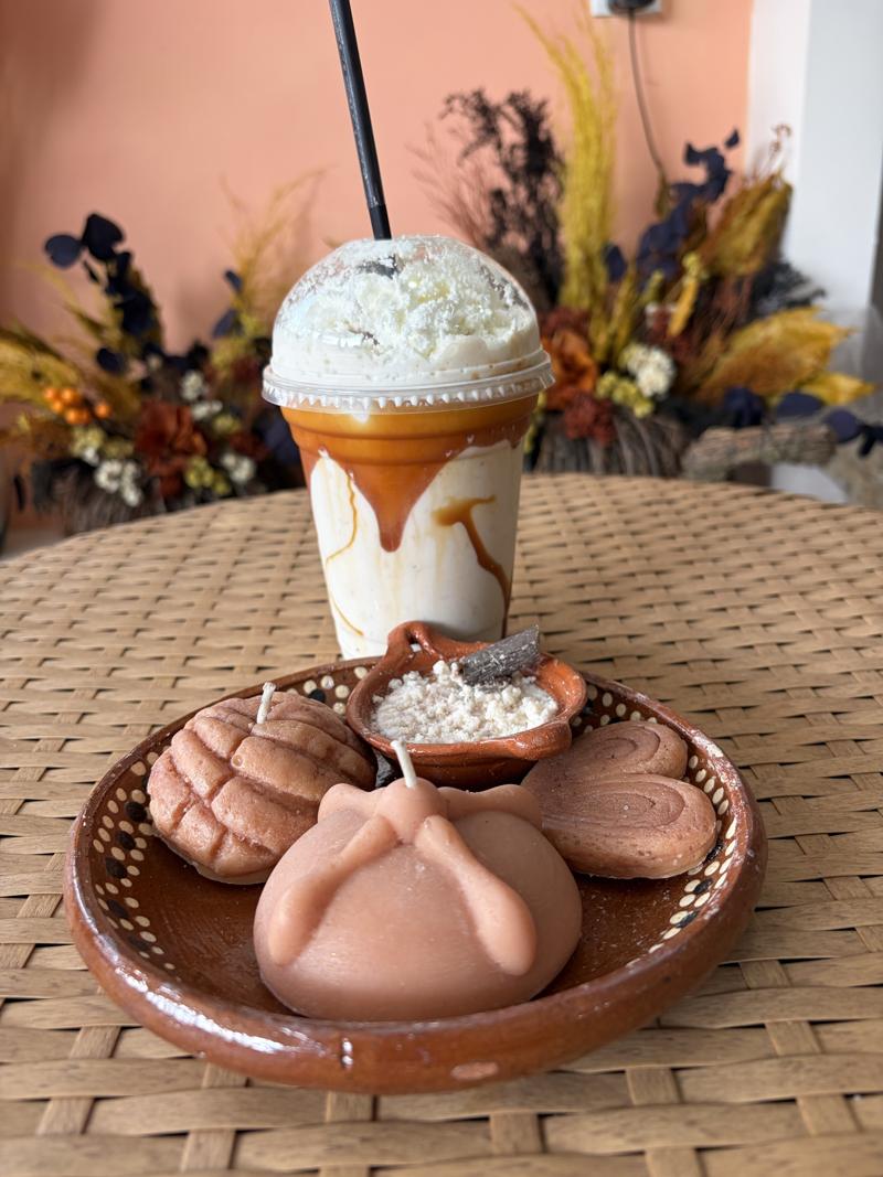 Mesa de Vel-Aura con velas de pan dulce, un frappé y flores secas al fondo